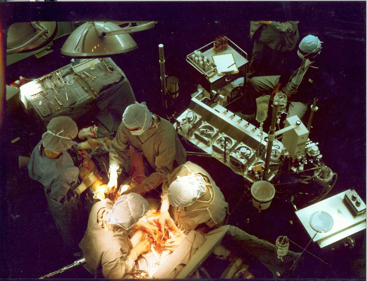 Early in a coronary artery bypass operation, during vein harvesting from the legs (left of image) and the establishment of cardiopulmonary bypass by placement of an aortic cannula (bottom of image). The perfusionist and heart-lung machine are on the upper right. The patient's head (not seen) is at the bottom.